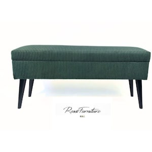 May include: A rectangular storage bench upholstered in a dark green corduroy fabric with vertical ribbed texture. The bench features a hinged lid and is supported by four tapered black wooden legs. The text Rossi Furniture M.A.I. is visible.