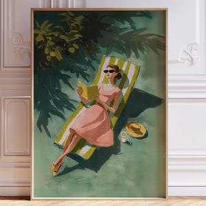 May include: A framed art print depicts a woman in a pink dress reading a book while reclining on a striped lounge chair. A yellow hat and drink sit nearby. The scene is set outdoors under a tree, with a green and yellow color scheme.