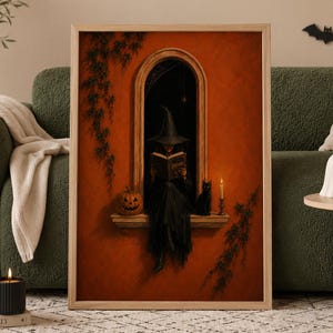 May include: A framed wall art print featuring a witch in a black hat and dress sitting in an arched window, reading a book. The scene includes a jack-o'-lantern, a black cat, and a lit candle against a deep orange wall with climbing ivy vines.