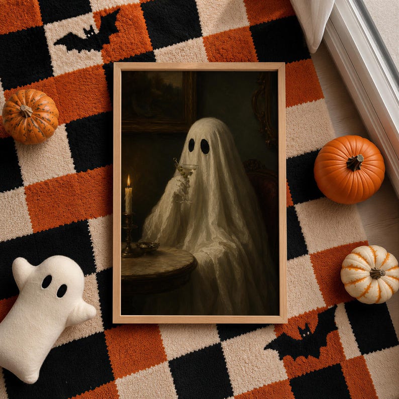 May include: A framed wall art print featuring a ghost draped in a white sheet, sitting at a round table with a lit candle and holding a glass. The artwork is displayed on a checkered rug with orange, black, and white squares, decorated with pumpkins.