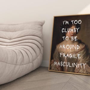 May include: A framed print of a woman in a white dress with the text "I'm too clumsy to be around fragile masculinity" written in white paint.