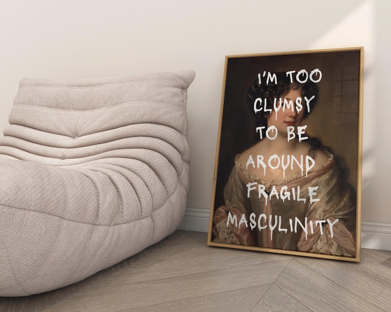 May include: A framed print of a woman in a white dress with the text "I'm too clumsy to be around fragile masculinity" written in white paint.