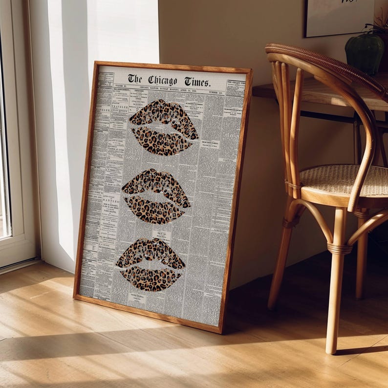 May include: A framed print with three leopard print lips on a vintage newspaper background. The wooden frame displays the text "The Chicago Times". The artwork is leaning against a wall, with a wooden chair visible in the background.