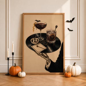 Op de afbeelding: Een ingelijste muurkunstprint met een skeletthand in een zwarte mouw die een zwarte vinylplaat als dienblad vasthoudt. Op de plaat staan een cocktailglas met een vleermuisgarnering, een glas met een schijfje sinaasappel, een kom met oogbollen en een servet.
