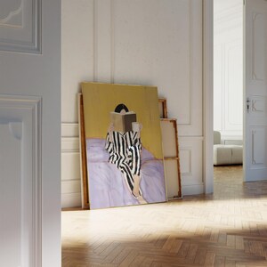 May include: An original painting depicts a person in black and white striped pajamas reading a book while sitting on a bed. The painting has a gold background and is leaning against a wall in a room with a wooden floor.
