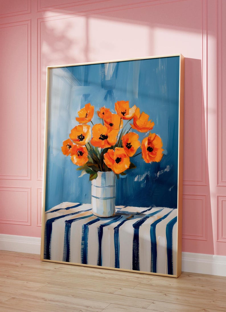 May include: A framed painting featuring orange poppies in a white vase with blue stripes, set against a blue backdrop. The vase rests on a table with blue and white stripes. The frame is gold, and the wall is pink.