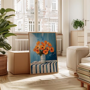 May include: A framed painting depicting orange poppies in a white vase with blue stripes, placed on a blue and white striped table. The background is light blue, with a wooden frame. The painting is in a bright room with a large window.