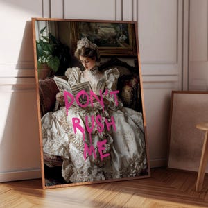 May include: A woman in a white dress with gold embroidery sits on a couch and reads a newspaper. The words "Don't Rush Me" are written in pink spray paint across the dress.