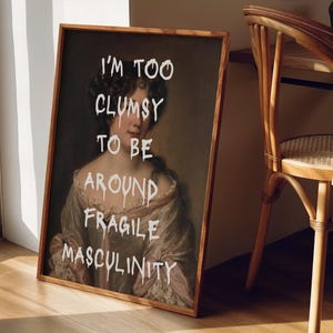 May include: A framed print of a painting of a woman with the text "I'm too clumsy to be around fragile masculinity" superimposed on the image.