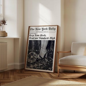 K&ouml;nnte beinhalten: Ein gerahmter Schwarz-Wei&szlig;-Druck einer Zeitungsseite mit dem Titel "The New York Daily". Die Schlagzeile lautet "Keep Your Heels, Head and Standards High". Das Bild zeigt Frauenbeine in High Heels und eine Discokugel.