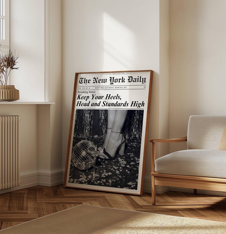 K&ouml;nnte beinhalten: Ein gerahmter Schwarz-Wei&szlig;-Druck einer Zeitungsseite mit dem Titel "The New York Daily". Die Schlagzeile lautet "Keep Your Heels, Head and Standards High". Das Bild zeigt Frauenbeine in High Heels und eine Discokugel.