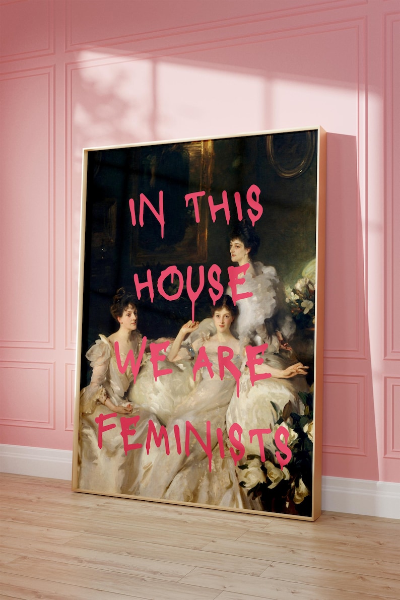 May include: A painting of three women in white dresses with the words "In this house we are feminists" written in pink spray paint over the image.