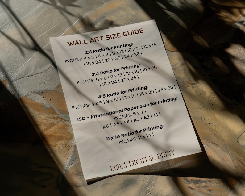 May include: A white card with a black and grey text guide for wall art sizes. The guide includes different ratios for printing, such as 2:3, 3:4, and 4:5, with corresponding inch measurements. It also includes international paper sizes for printing, such as A6, A5, A4, A3, A2, and A1, with corresponding inch measurements. The card also includes a 11 x 14 ratio for printing with corresponding inch measurements. The card is titled "Wall Art Size Guide" and has the text "Leila Digital Print" at the bottom.