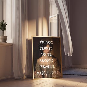 May include: A framed print of a portrait of a woman with a gold frame. The portrait is painted in a traditional style and the woman is wearing a white dress. The text "I'm too clumsy to be around fragile masculinity" is written in white paint over the portrait.