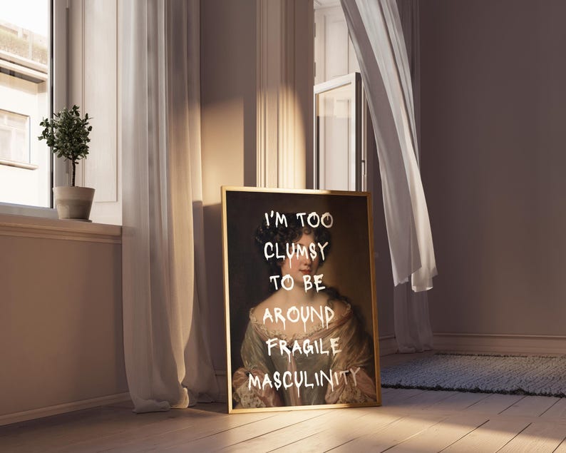 May include: A framed print of a portrait of a woman with a gold frame. The portrait is painted in a traditional style and the woman is wearing a white dress. The text "I'm too clumsy to be around fragile masculinity" is written in white paint over the portrait.