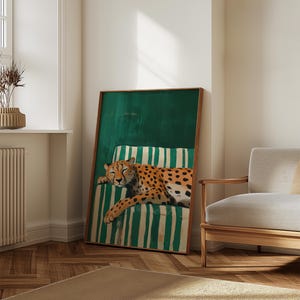 May include: A framed art print featuring a sleeping cheetah on a green and white striped cushion. The cheetah has orange fur with black spots. The artwork is in a wooden frame and leans against a white wall.