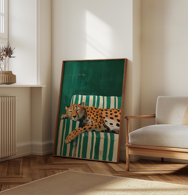 May include: A framed art print featuring a sleeping cheetah on a green and white striped cushion. The cheetah has orange fur with black spots. The artwork is in a wooden frame and leans against a white wall.