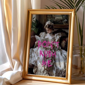 May include: A framed print of a woman in a white dress reading a book. The print has the words "DON'T RUSH ME" written in pink on it.