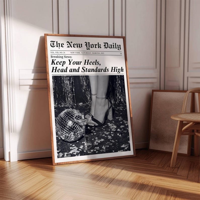 K&ouml;nnte beinhalten: Ein gerahmter Schwarz-Wei&szlig;-Druck einer Zeitungsseite mit dem Titel "The New York Daily". Die Schlagzeile lautet "Keep Your Heels, Head and Standards High". Das Bild zeigt eine Discokugel und High Heels.