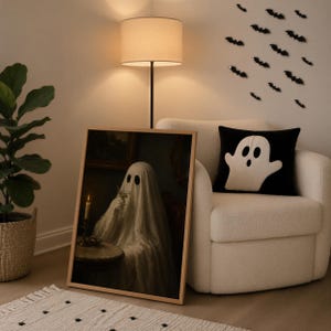 May include: A framed rectangular wall art print featuring a ghost draped in a white sheet sitting at a table with a lit candle, placed next to a white armchair with a black throw pillow displaying a white ghost graphic and wall bat decals.