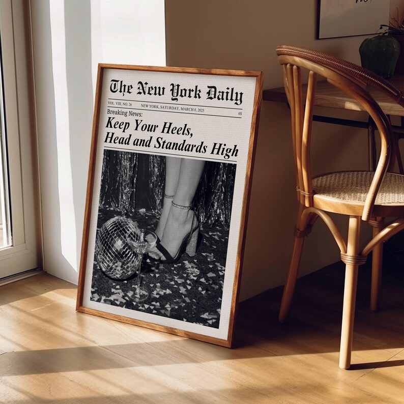 K&ouml;nnte beinhalten: Ein gerahmter Druck, der einer Zeitungsseite &auml;hnelt. Die Schlagzeile lautet "The New York Daily" mit der Eilmeldung: "Keep Your Heels, Head and Standards High." Das Bild zeigt Beine in High Heels und eine Discokugel.