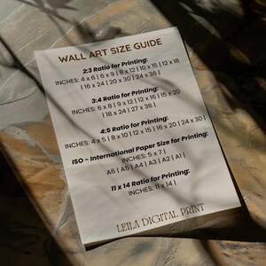 May include: A white card with a black and gray text guide for wall art sizes. The guide includes different ratios for printing, such as 2:3, 3:4, and 4:5, with corresponding inch measurements. It also includes international paper sizes for printing, such as A6, A5, A4, A3, A2, and A1, with corresponding inch measurements. The card also includes a 11 x 14 ratio for printing with corresponding inch measurements. The card is titled "Wall Art Size Guide" and has the text "Leila Digital Print" at the bottom.