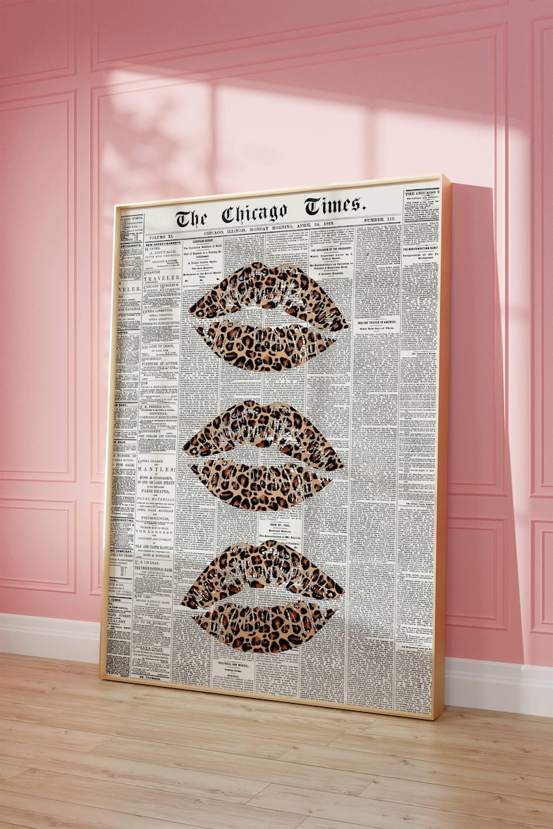 May include: A framed print with three leopard print lip designs set against a vintage newspaper background. The newspaper is titled "The Chicago Times." The artwork is in a gold frame, displayed against a pink wall.