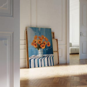 May include: An oil painting depicting orange flowers in a vase with blue and white stripes, set on a table with a blue and white striped cloth. The background is a blue sky. The painting is leaning against a wall.