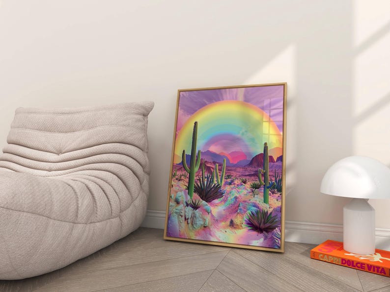 May include: A framed print of a desert landscape with a rainbow arching over the scene. The desert is a vibrant pink and purple with green cacti and plants.