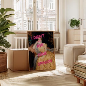 May include: A framed print of a painting of a woman in a yellow dress and a fur stole. The woman is holding a cup and blowing a bubble. The text "I didn't ask your opinion" is written in pink letters over the image.