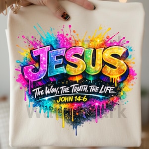 May include: A cream-colored fabric item featuring a vibrant, multi-colored paint splatter design. The word JESUS is printed in large, bold, gradient-colored letters, followed by the text The Way, The Truth, The Life and John 14:6 in white.