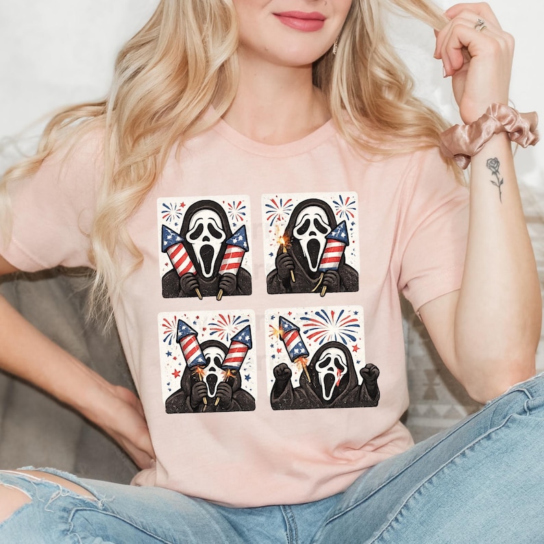 K&ouml;nnte beinhalten: Hellrosa T-Shirt mit einem sich wiederholenden 2x2 Rastermuster. Jedes Feld zeigt die Ghostface-Maske aus den Scream-Filmen, die Feuerwerk in den Farben der amerikanischen Flagge h&auml;lt.