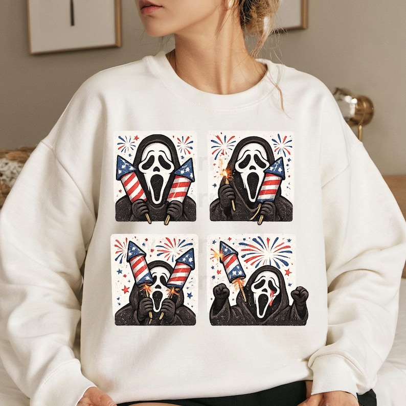 K&ouml;nnte beinhalten: Wei&szlig;es Sweatshirt mit einem Aufdruck der Ghostface-Maske aus den Scream-Filmen, die Feuerwerksk&ouml;rper mit der amerikanischen Flagge h&auml;lt. Das Design wiederholt sich in vier Quadraten mit verschiedenen Feuerwerksdarstellungen.