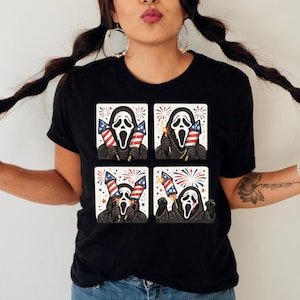 K&ouml;nnte beinhalten: Schwarzes T-Shirt mit einem viergeteilten Grafikdesign der Ghostface-Maske, die Feuerwerk und amerikanische Flaggen h&auml;lt. Das Design verwendet rote, wei&szlig;e und blaue Farben mit einem festlichen Thema.