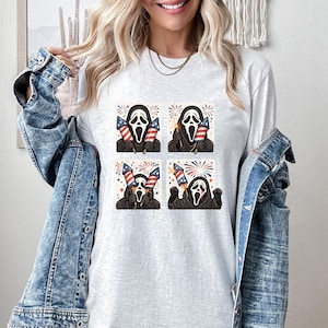 K&ouml;nnte beinhalten: Ein hellgraues Langarmshirt mit einem viergeteilten Design der Ghostface-Maske, die amerikanische Flaggen und Feuerwerk h&auml;lt. Das Design verwendet rote, wei&szlig;e und blaue Farben und feiert den Unabh&auml;ngigkeitstag.