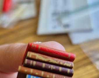 May include: A stack of five miniature books with red, brown, and blue covers. The books are arranged in a stack with the red book on top and the blue book on the bottom.