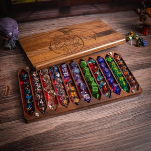 May include: Wooden dice box with a dragon and dice design. The box is open, revealing a variety of colorful polyhedral dice. The dice are arranged in individual slots within the box, showcasing their different colors and patterns.