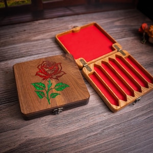 May include: A wooden box with a red rose design on the lid. The box is open and has a red felt interior with five slots for holding items.