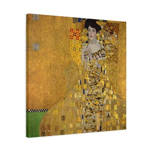 May include: A canvas print of a Gustav Klimt painting, featuring a woman in a long, ornate gold dress. The artwork has a gold background with geometric and organic patterns. The woman has dark hair and is wearing a jeweled necklace.