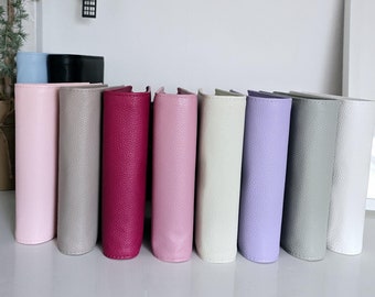 May include: A row of ten different colored leather-bound journals or notebooks. The colors are pink, gray, burgundy, light pink, cream, lavender, gray, white, black, and light blue.