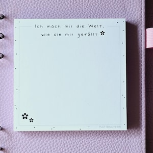Könnte beinhalten: Ein hellblauer Haftnotiz mit schwarzem Rand und schwarzen Punkten. Der Notiz enthält den Text "Ich mach mir die Welt, wie sie mir gefällt" und eine kleine Blumengrafik.