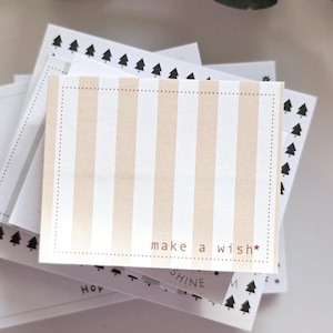 Könnte beinhalten: Ein Stapel Karten mit beigen und weißen Streifen und dem Aufdruck "make a wish". Die Karten haben einen gepunkteten Rand und sind von anderen Karten mit kleinen Baumdesigns umgeben.