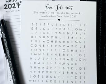 May include: A white square card featuring a German word search puzzle titled Dein Jahr 2027 with the text Die ersten 3 Wörter, die Du entdeckst, beschreiben Dein Jahr 2027. A black pen with the text NEW YEAR, NEW CHANCES, HELLO 2027 is placed beside it.