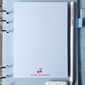 May include: A light blue planner with a lined notepad, a white pencil, and a cherry-themed eraser. The notepad has a cherry graphic and the text "Sweet moments." The pencil also has the text "Sweet moments."