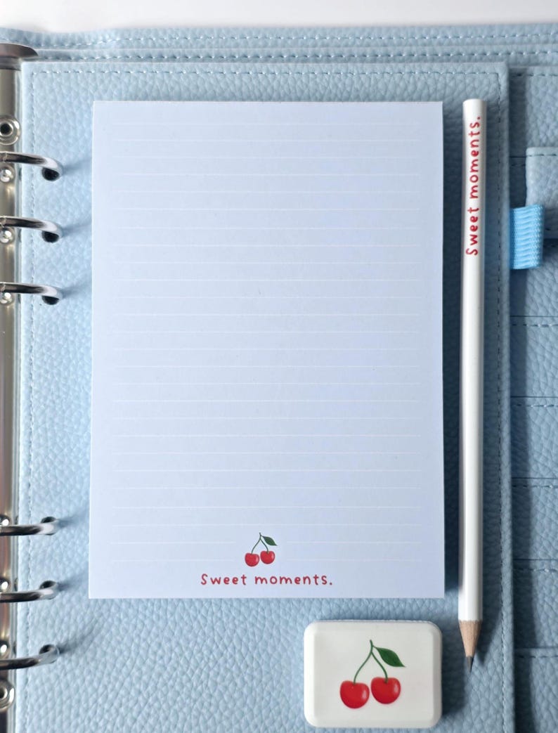 May include: A light blue planner with a lined notepad, a white pencil, and a cherry-themed eraser. The notepad has a cherry graphic and the text "Sweet moments." The pencil also has the text "Sweet moments."