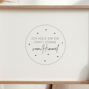 Könnte beinhalten: Ein gerahmter Druck mit einem hellen Holzrahmen. Der Druck hat einen weißen Hintergrund mit einem kreisförmigen Design in der Mitte. Das Design enthält Text und kleine Sterne. Der Text lautet "ICH HOLE DIR DIE (ZIMT) STERNE vom Himmel."