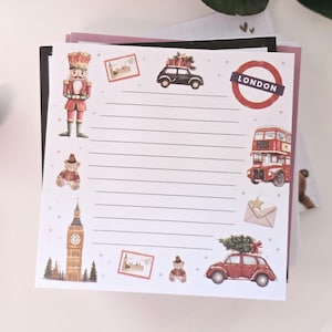 Könnte beinhalten: Ein Stapel Notizblöcke mit London-Motiv. Der oberste Notizblock zeigt Illustrationen eines Nussknackers, Teddybären, Big Ben, eines Doppeldeckerbusses und Autos mit Weihnachtsbäumen. Der Notizblock hat einen weißen Hintergrund mit einem London-Stempel.