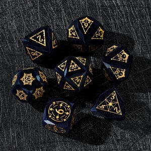 Puede incluir: Un conjunto de siete dados poliédricos azul marino con números y símbolos dorados, perfectos para juegos de rol. Los dados están colocados sobre una superficie texturizada de color gris oscuro.