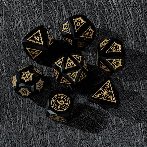 May include: A collection of seven black polyhedral dice featuring gold numerals and decorative patterns. The dice are displayed on a dark, textured surface, ideal for role-playing games.