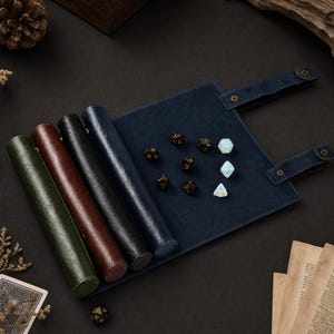 May include: A dark blue leather dice rolling mat with a matching dice storage case. The mat is open, displaying several dice in various colors and shapes. Four rolled-up cases in green, brown, black, and blue are visible.